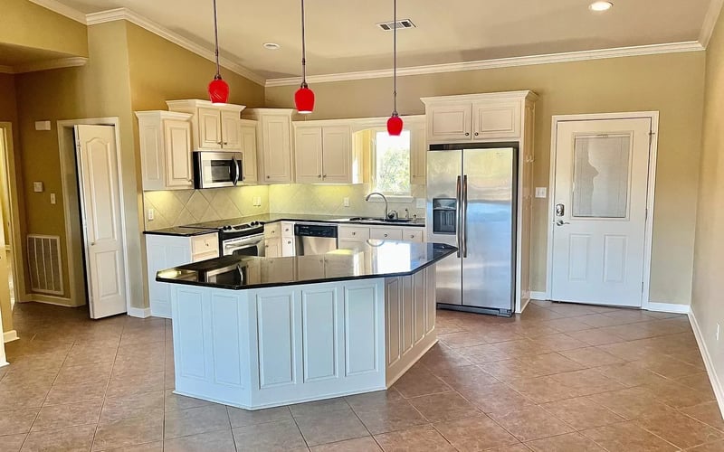 Kitchen with white cabinets, black granite island, and red pendants